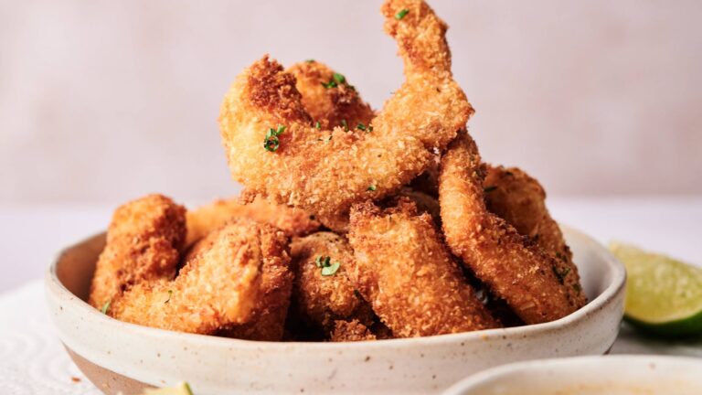 A bowl filled with golden-brown breaded shrimp garnished with chopped herbs, with a wedge of lime visible on the side.