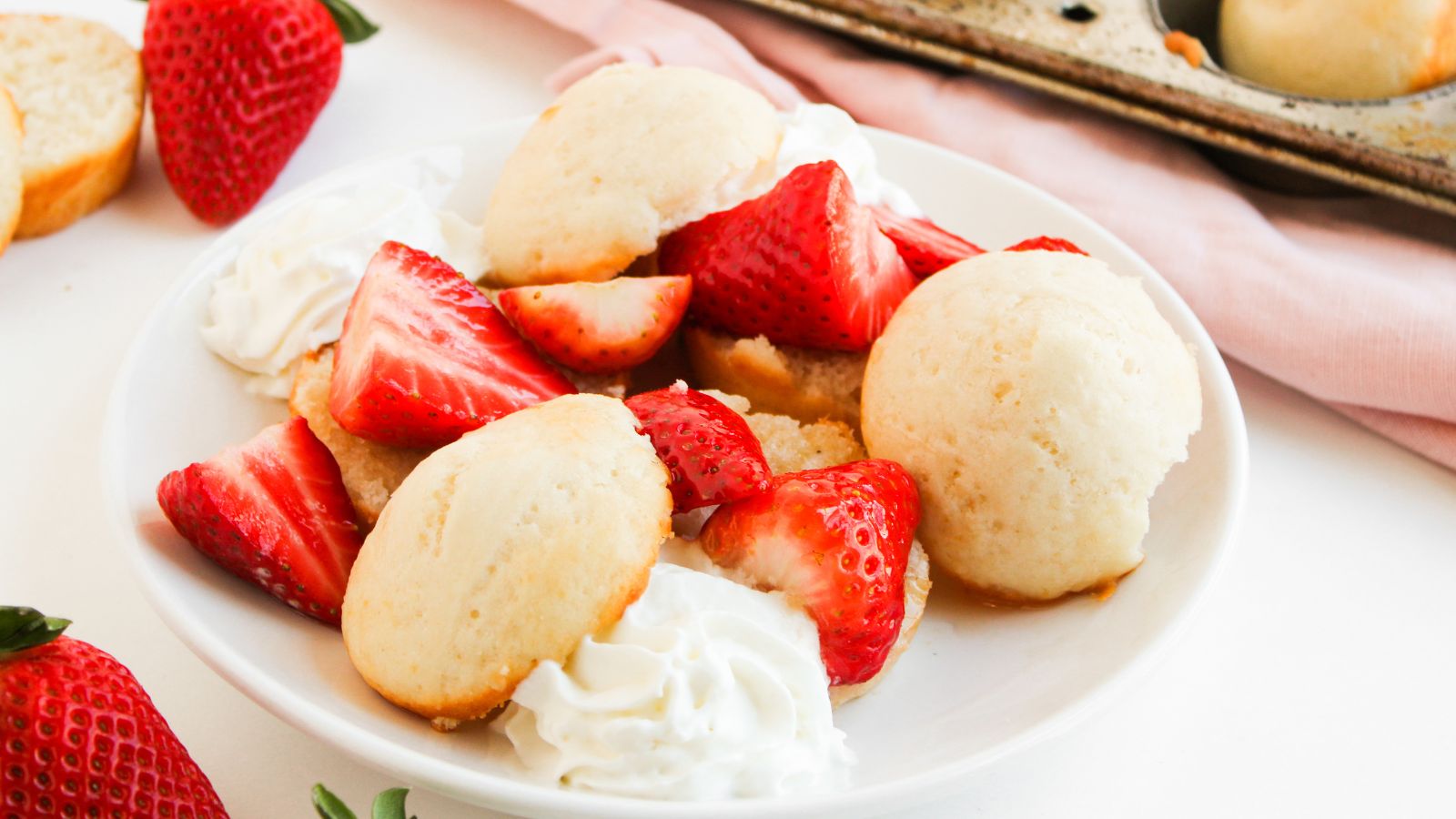 A plate of strawberry shortcake with sliced strawberries, dollops of whipped cream, and small round shortcakes on a white plate.
