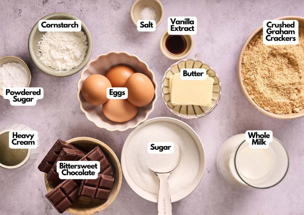 An overhead view of labeled Chocolate Cream Pie ingredients in bowls, including eggs, sugar, butter, crushed graham crackers, whole milk, bittersweet chocolate, heavy cream, powdered sugar, cornstarch, salt, and vanilla extract.