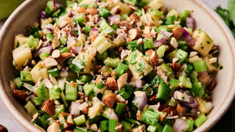 A bowl of chopped salad featuring celery, apples, red onion, fresh herbs, and chopped almonds.