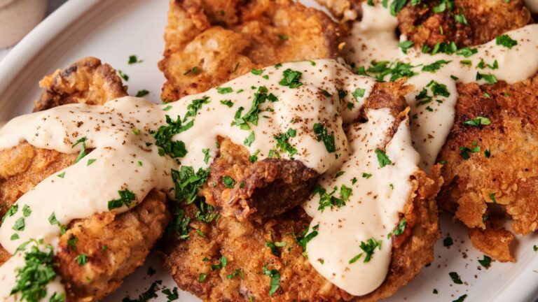 Plate of breaded and fried meat cutlets topped with creamy white gravy and garnished with chopped parsley.