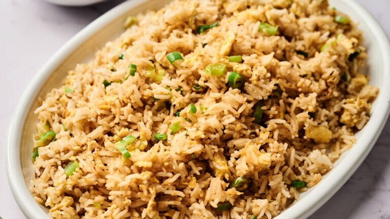 A white oval dish filled with fried rice mixed with chopped green onions and scrambled eggs.