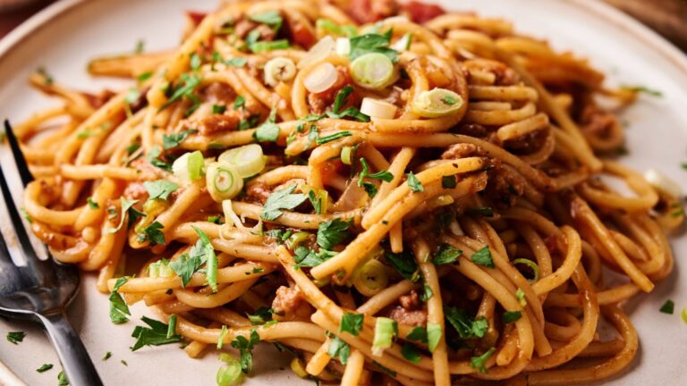 A plate of spaghetti with meat sauce, garnished with chopped green onions and parsley, with a fork on the side.