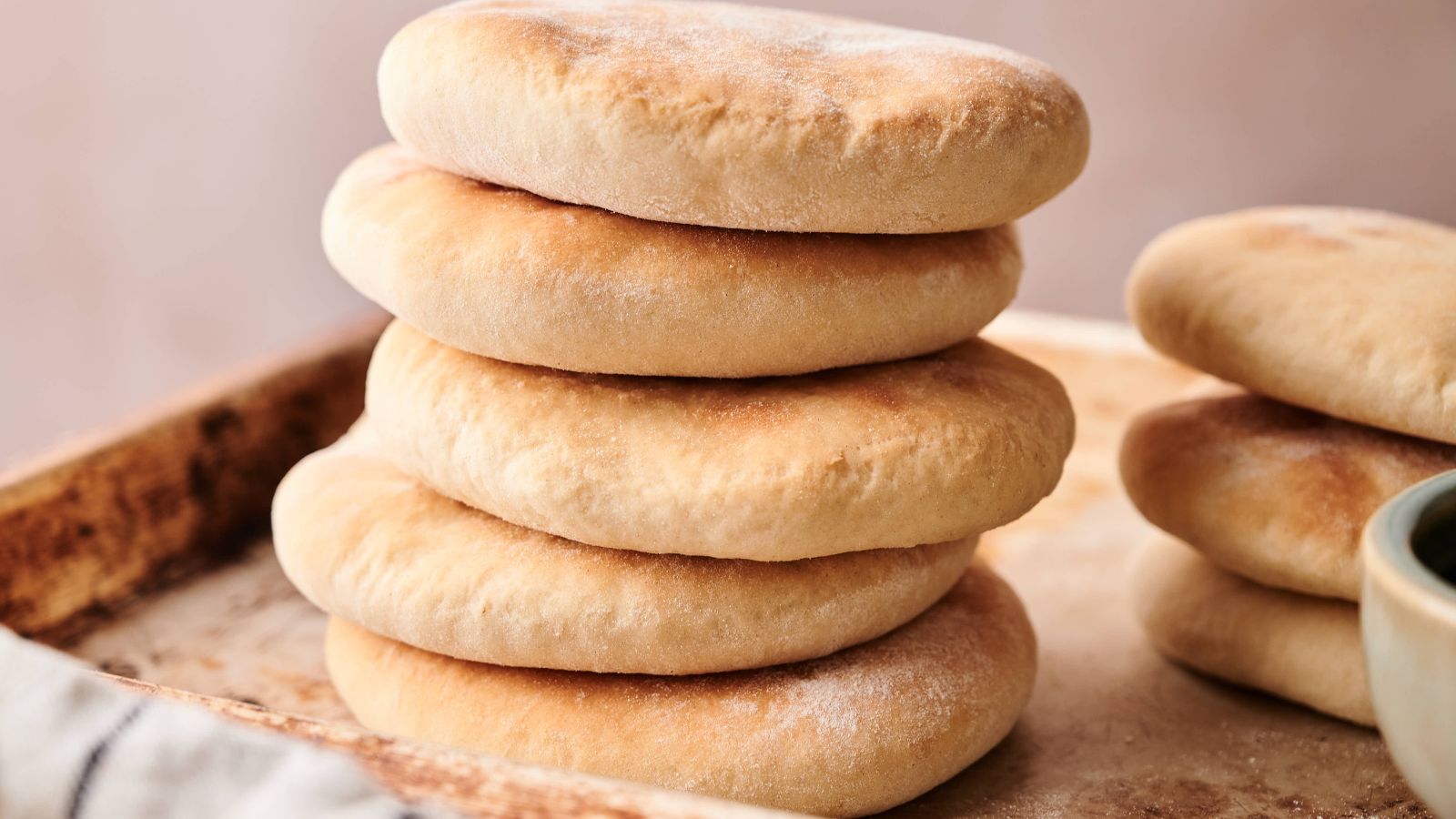 A stack of six round, golden-brown pita breads sits on a baking tray, with more pita breads visible to the side.
