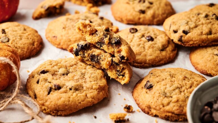 A close-up of several chocolate chip cookies on parchment paper, with one cookie broken in half to show the chocolate chips inside.