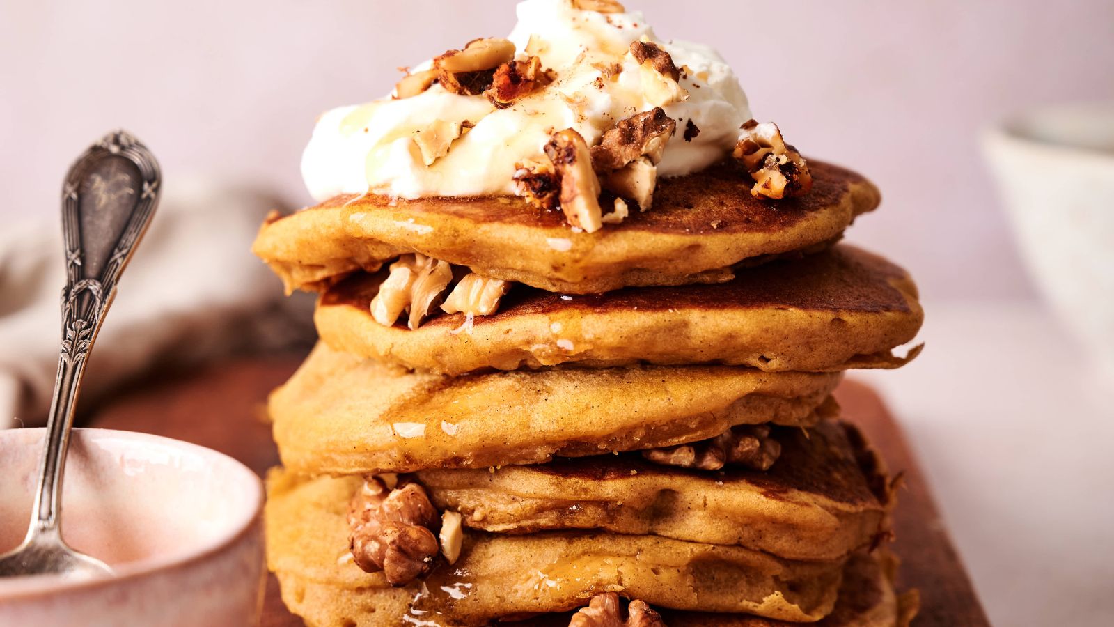 A stack of pancakes with whipped cream and nuts.