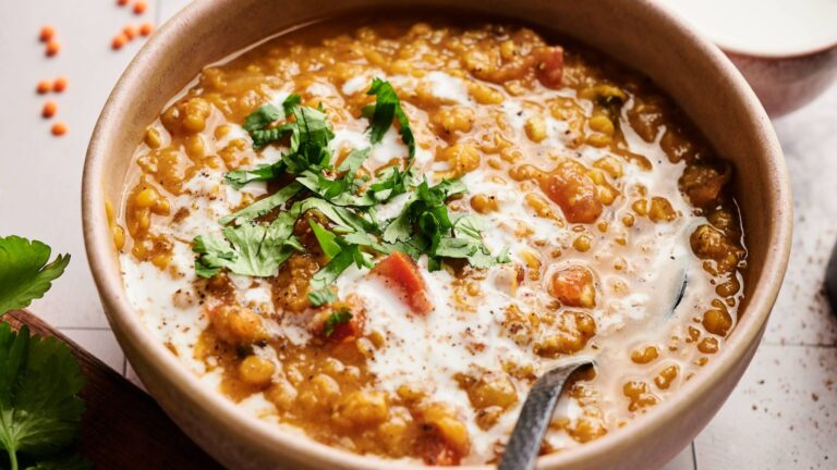 A bowl of lentil curry garnished with chopped cilantro and a swirl of cream, with a spoon in the bowl.