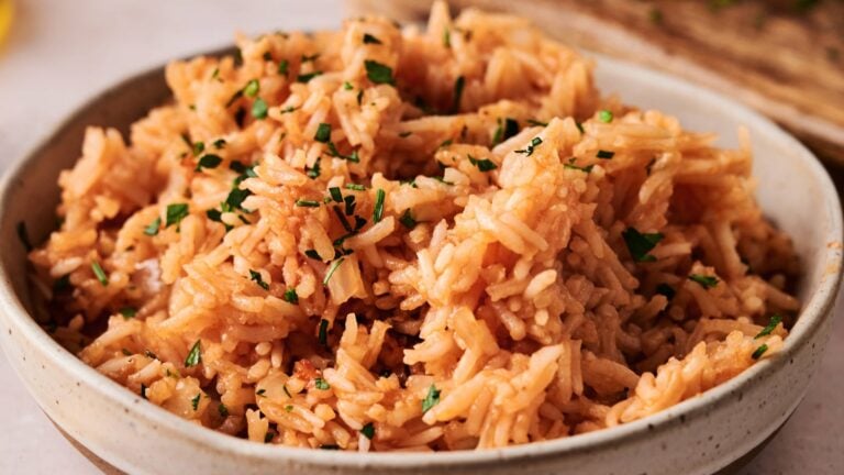 A bowl of cooked Mexican rice garnished with chopped parsley.