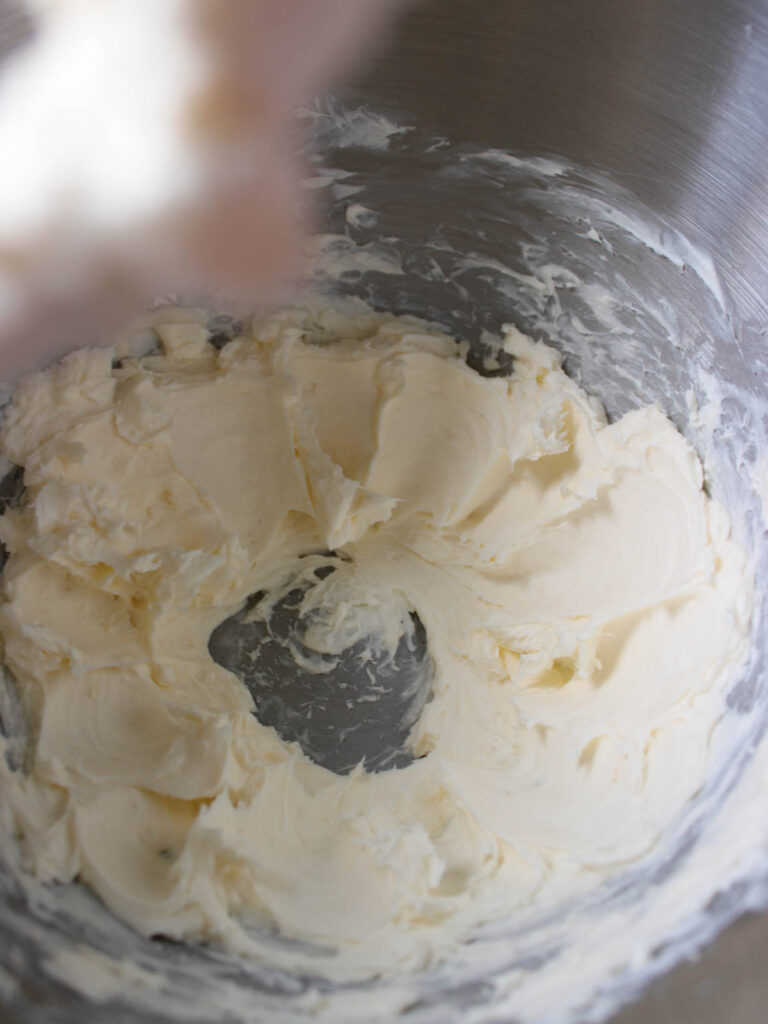 Creamy, whipped butter and sugar mixture in a metal mixing bowl, ready to be folded into Pumpkin Cupcakes, with visible traces from a mixing attachment around the sides.