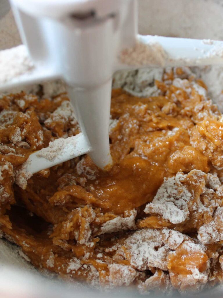 Electric mixer blending orange batter and flour in a mixing bowl, creating the perfect base for delicious Pumpkin Cupcakes.