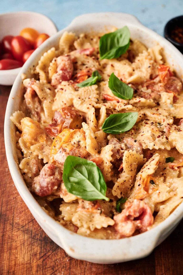 Baked Feta Pasta bowtie noodles with tomatoes, creamy sauce, and fresh basil leaves, served in a white oval dish on a wooden surface.