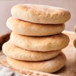 A stack of round, flat pita bread sits on a baking tray.