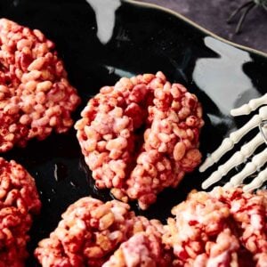 Halloween Rice Krispie Brains shaped like brains, coated in pink and red, are arranged on a black plate with a white decorative spider web design&mdash;perfectly sweet treats for your spooky celebration.