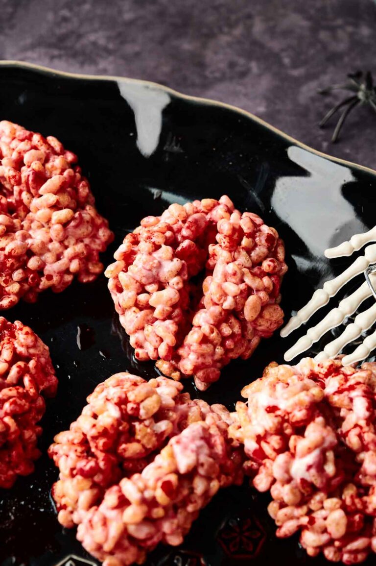 Halloween Rice Krispie Brains shaped like brains, coated in pink and red, are arranged on a black plate with a white decorative spider web design—perfectly sweet treats for your spooky celebration.
