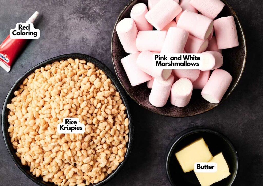 Bowls containing ingredients for Halloween Rice Krispies Brains&mdash;Rice Krispies, pink and white marshmallows, butter, and a tube of red coloring&mdash;sit on a dark countertop.