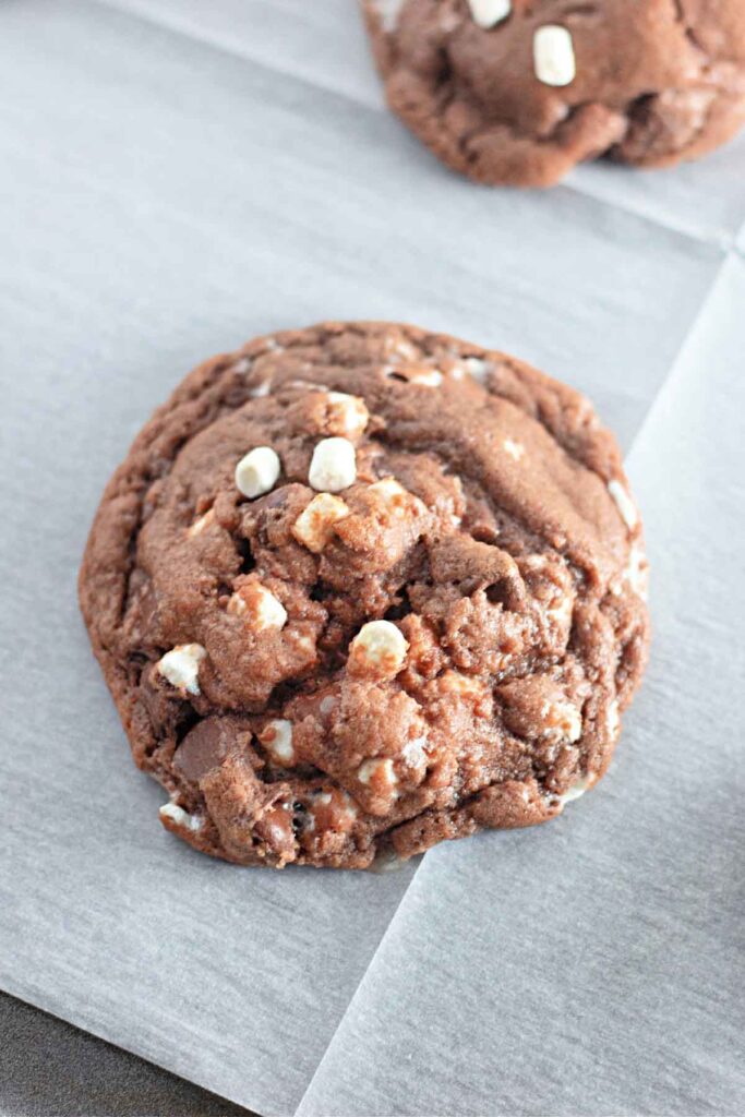 A double chocolate Hot Cocoa Cookie with white chocolate chips rests on a sheet of parchment paper.