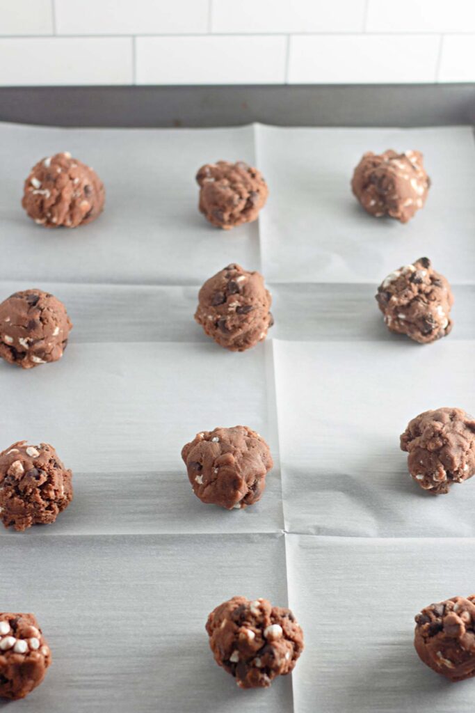 Twelve scoops of Hot Cocoa Cookies dough are evenly spaced on a parchment-lined baking sheet, ready for baking.