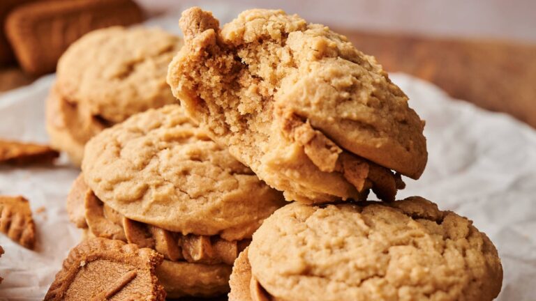A stack of peanut butter sandwich cookies, one with a large bite taken out, on parchment paper with cookie crumbs nearby.
