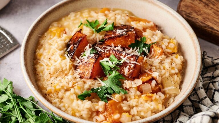 A bowl of creamy risotto topped with roasted pumpkin cubes, grated cheese, and fresh parsley.