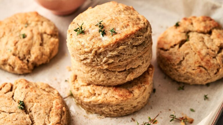 Four golden-brown biscuits rest on parchment paper, with fresh thyme sprinkled on top of two stacked in the center.