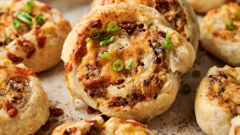 Close-up of savory pastry pinwheels topped with chopped green onions, featuring a golden, flaky crust and a cheesy, seasoned filling.