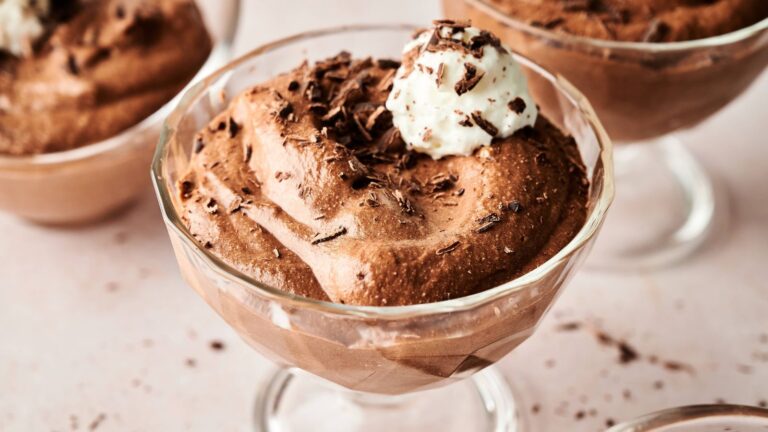 A glass dessert dish filled with chocolate mousse, topped with whipped cream and chocolate shavings.