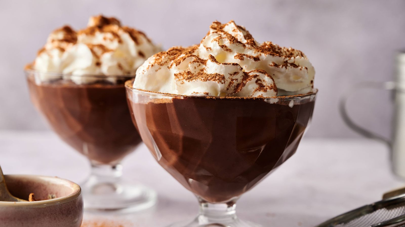 Two glass dessert cups filled with chocolate pudding, each topped with whipped cream and chocolate shavings.