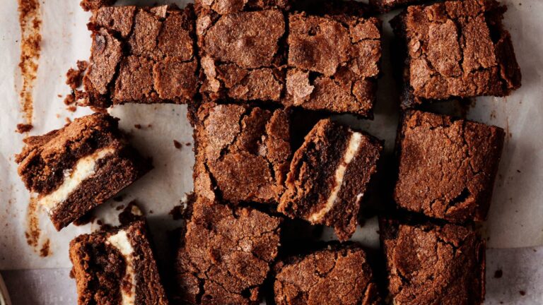 Sliced chocolate brownies with a cream cheese filling arranged on parchment paper.