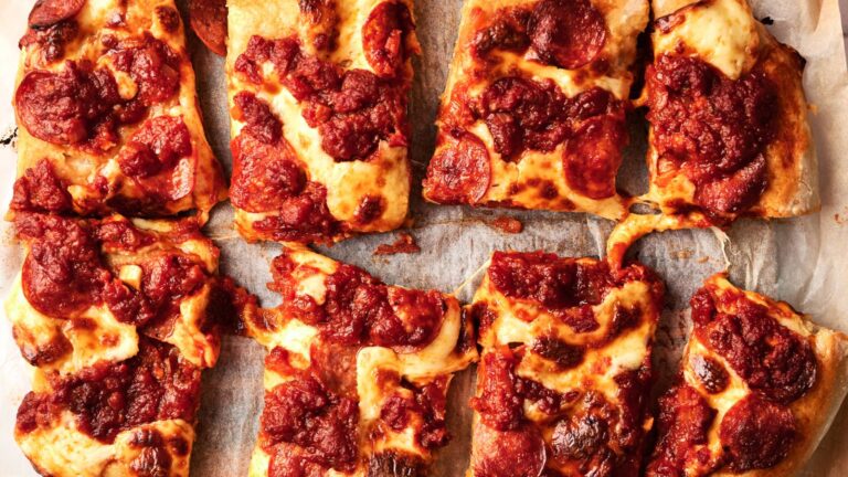 Eight rectangular slices of thick-crust pizza topped with tomato sauce, melted cheese, and pepperoni, arranged on parchment paper.