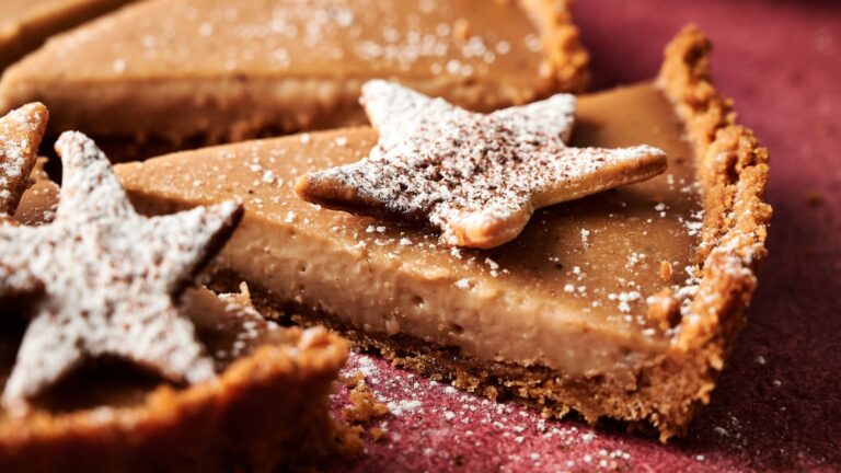 A close-up of a sliced pie with a crumb crust, topped with star-shaped cookies dusted with powdered sugar.