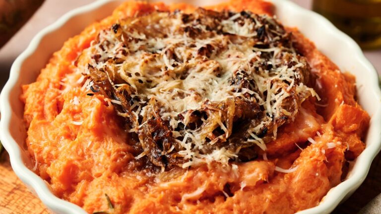 A bowl of mashed sweet potatoes topped with caramelized onions and grated cheese.