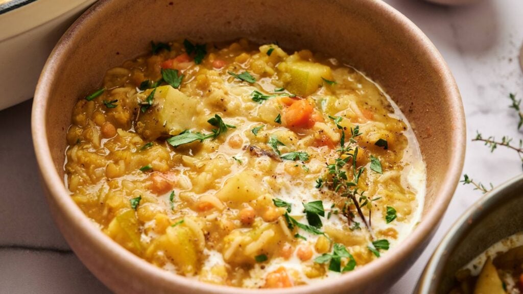 A bowl of thick lentil and vegetable stew topped with fresh herbs, featuring visible pieces of potato, carrot, and parsley.