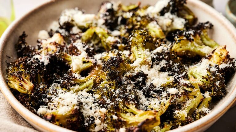 A bowl of roasted broccoli florets topped with grated parmesan cheese.