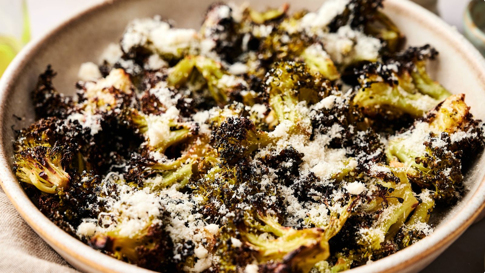 A bowl of roasted broccoli topped with grated cheese and seasoning.