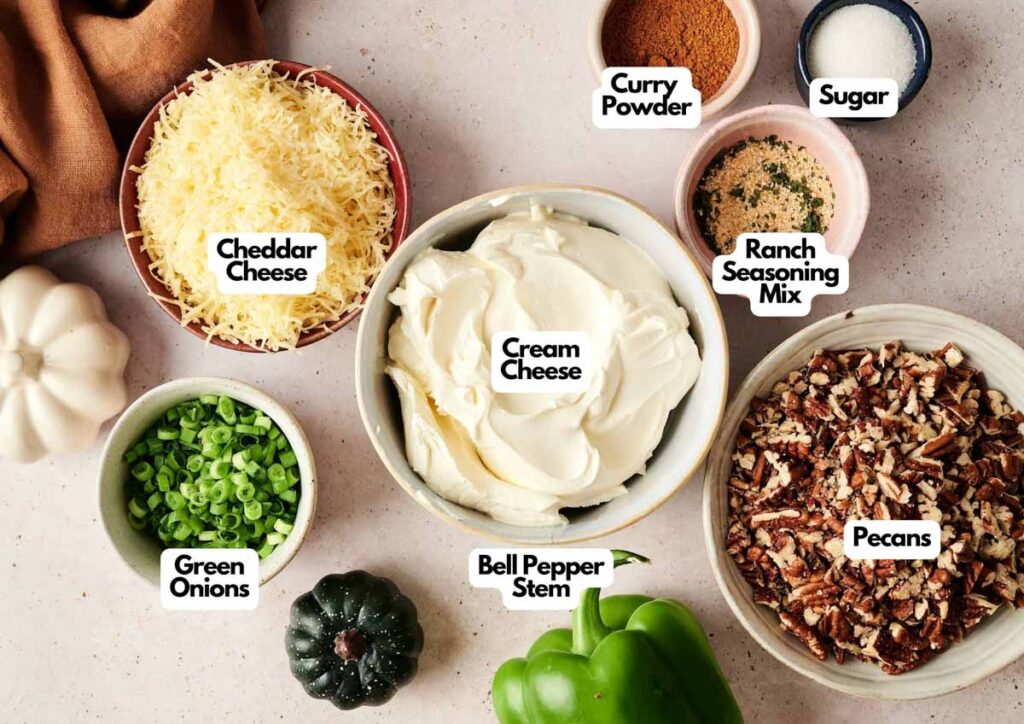 Ingredients for a Pumpkin-Shaped Cheeseball laid out in bowls: cheddar cheese, cream cheese, ranch seasoning mix, curry powder, sugar, green onions, bell pepper stem, and chopped pecans.
