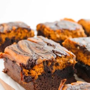 Pumpkin Spice Fudgy Brownies cut into squares, each with a marbled chocolate and peanut butter swirl on top, arranged on a wooden board lined with parchment paper.