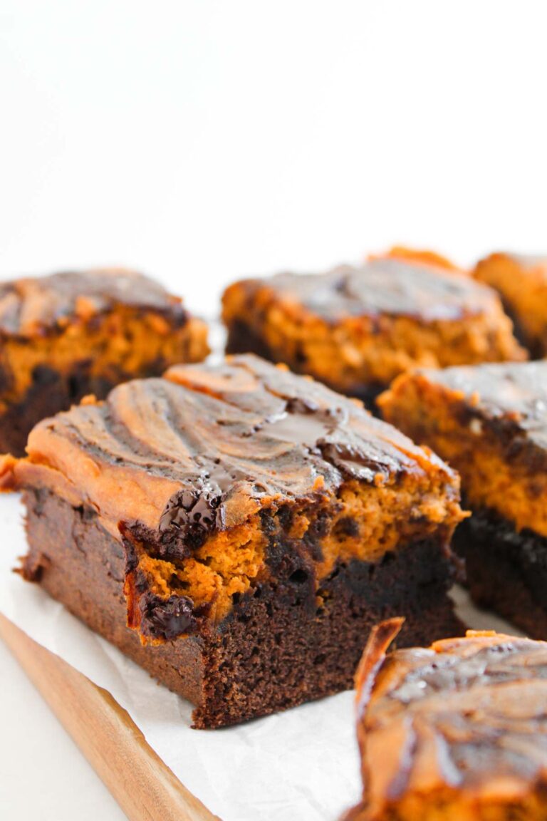 Pumpkin Spice Fudgy Brownies cut into squares, each with a marbled chocolate and peanut butter swirl on top, arranged on a wooden board lined with parchment paper.