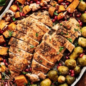 Sheet Pan Thanksgiving Dinner featuring sliced roasted chicken breasts, Brussels sprouts, sweet potatoes, pecans, and pomegranate seeds, all garnished with fresh herbs for a festive and easy holiday meal.