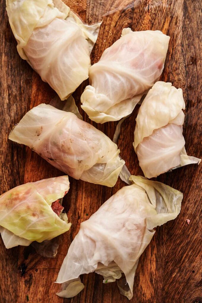 Six uncooked stuffed cabbage rolls filled with a savory meat mixture are arranged on a wooden surface.