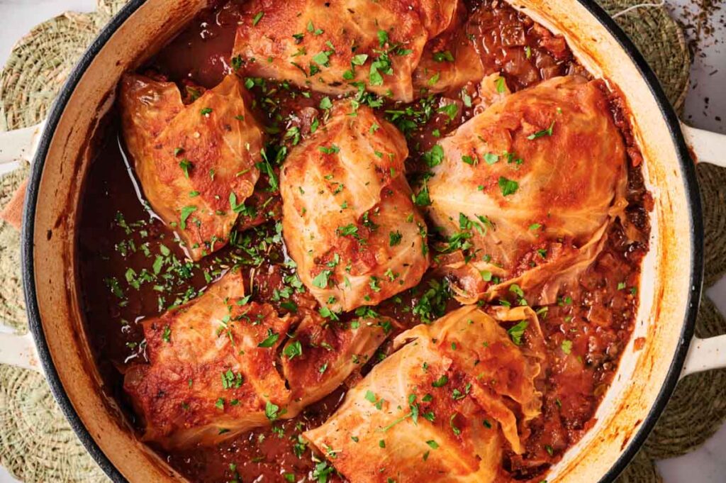 Stuffed Cabbage Rolls simmer in rich tomato sauce inside a pot, topped with chopped parsley for a comforting, classic dish.
