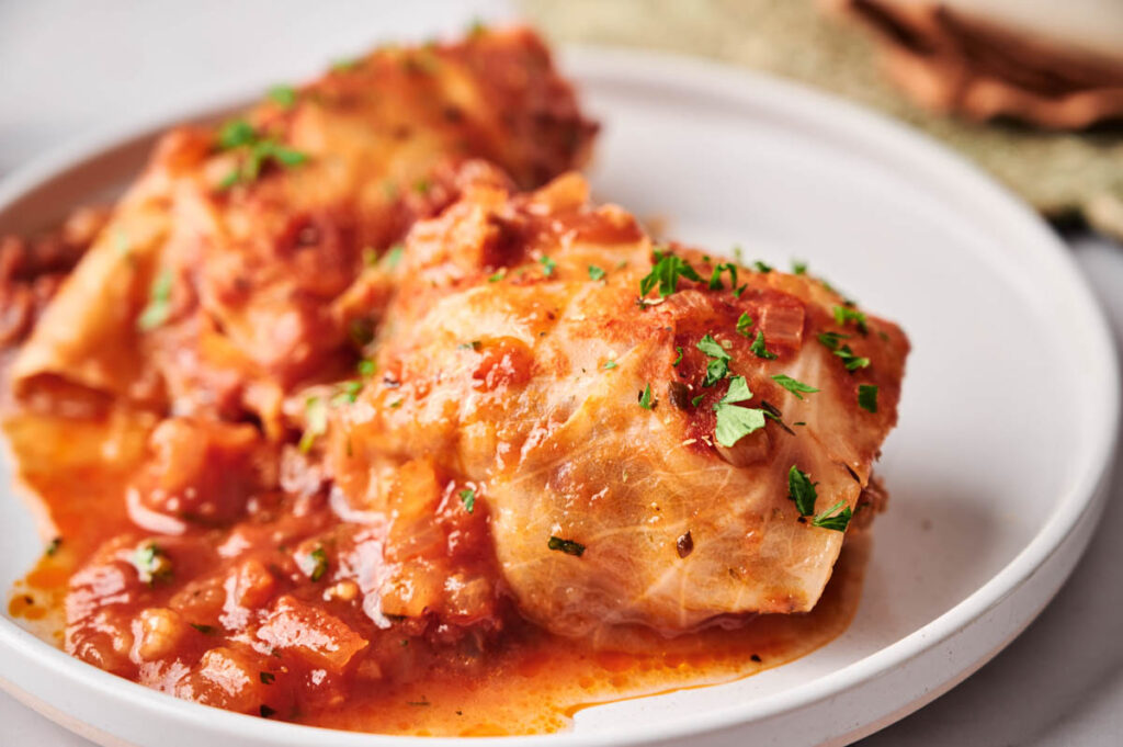 Two stuffed cabbage rolls topped with tomato sauce and chopped parsley are served on a white plate.