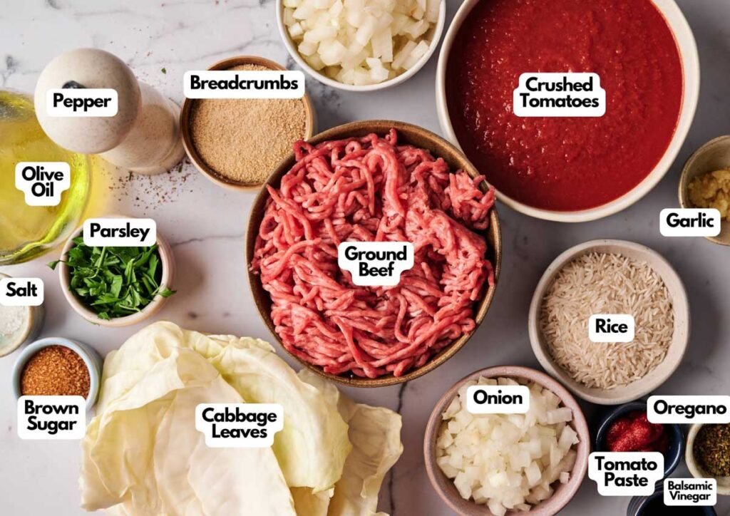 Various labeled ingredients for Stuffed Cabbage Rolls, including ground beef, cabbage leaves, rice, onion, garlic, parsley, pepper, olive oil, salt, brown sugar, breadcrumbs, oregano, tomato paste, balsamic vinegar, and crushed tomatoes.