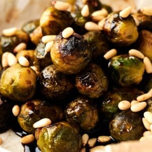 A plate of Brussels Sprouts with Balsamic Glaze is topped with crunchy pine nuts and roasted to perfection for a deliciously savory side dish.