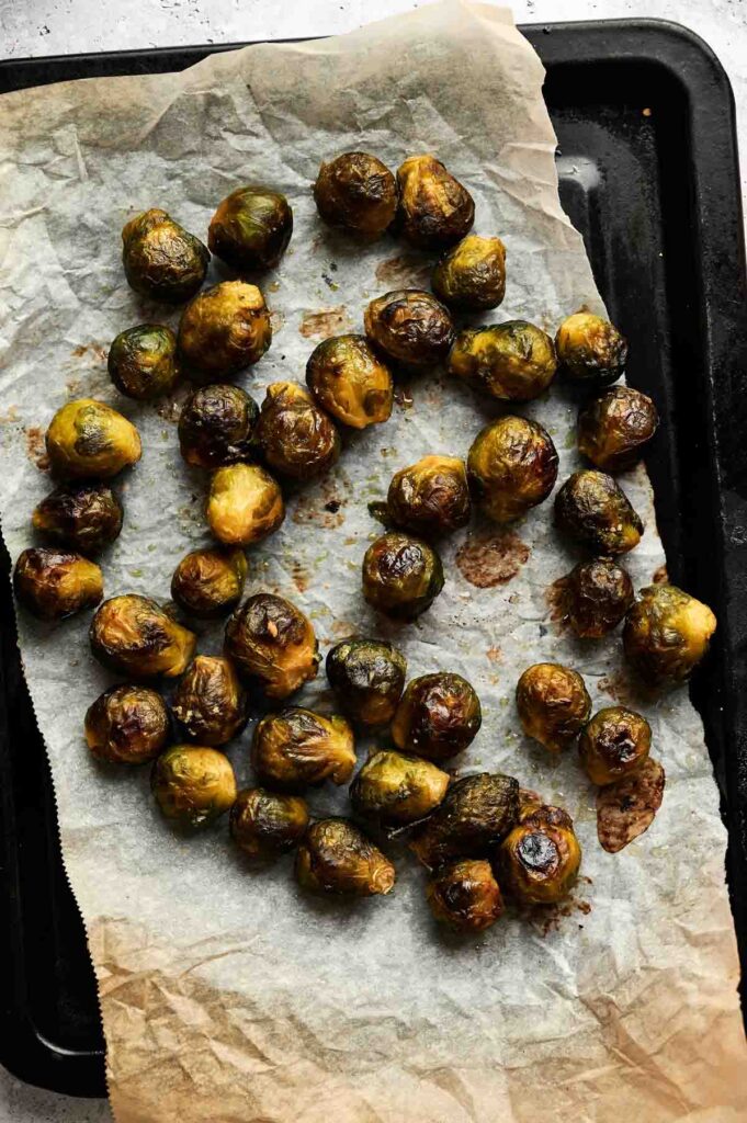 Brussels Sprouts with Balsamic Glaze are roasted to perfection and scattered on parchment paper atop a black baking tray.