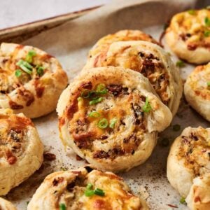 Baked Chicken Pinwheels filled with cheese and bacon, topped with chopped green onions, arranged on a parchment-lined baking tray.