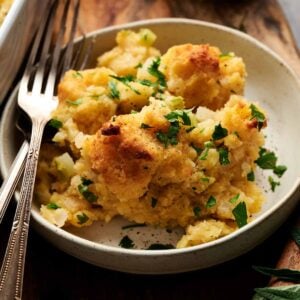 A plate of cornbread stuffing dressing garnished with chopped parsley, with three forks resting on the plate, set on a wooden surface.