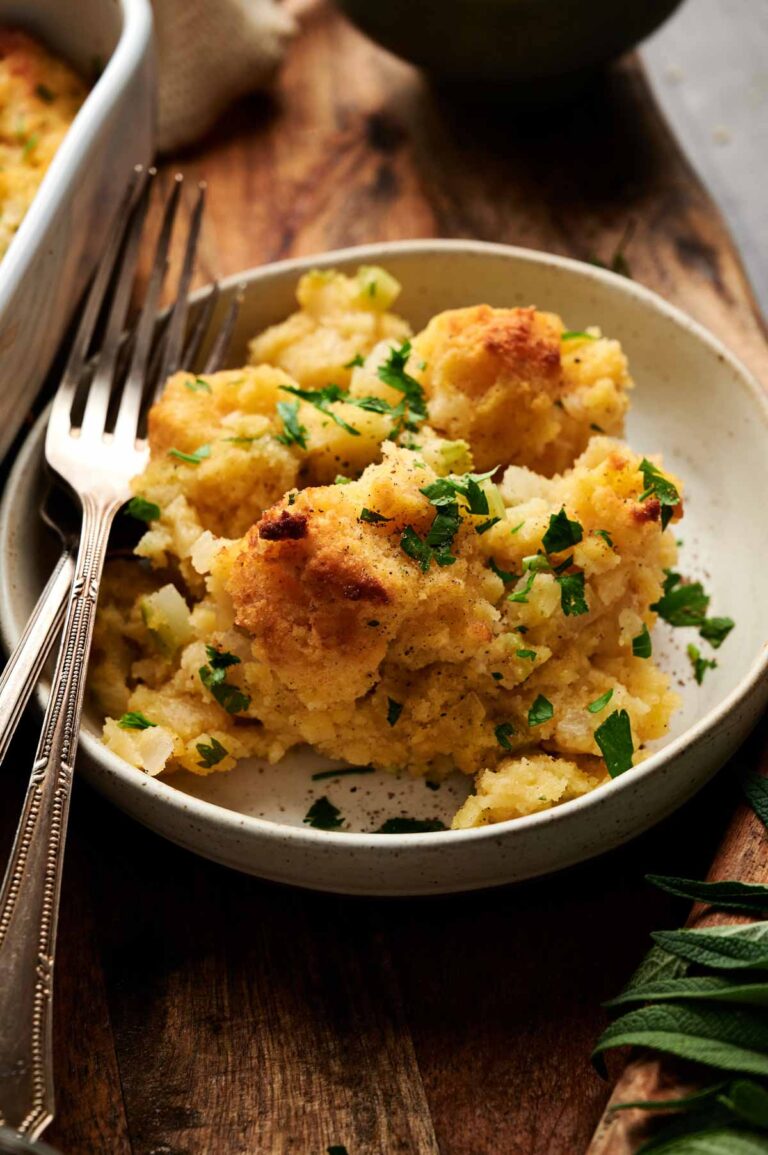 A plate of cornbread stuffing dressing garnished with chopped parsley, with three forks resting on the plate, set on a wooden surface.