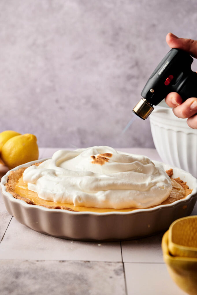 A person spraying a Lemon Meringue Pie.
