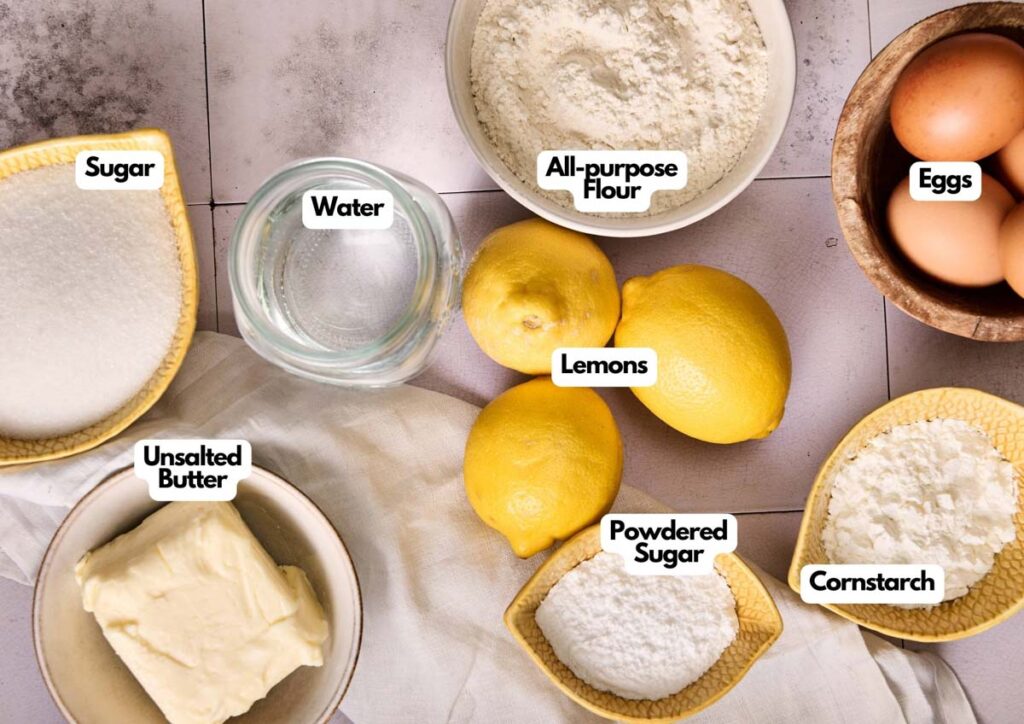 Top-down view of baking ingredients for Lemon Meringue Pie, including sugar, water, all-purpose flour, eggs, lemons, unsalted butter, powdered sugar, and cornstarch in separate bowls on a countertop.