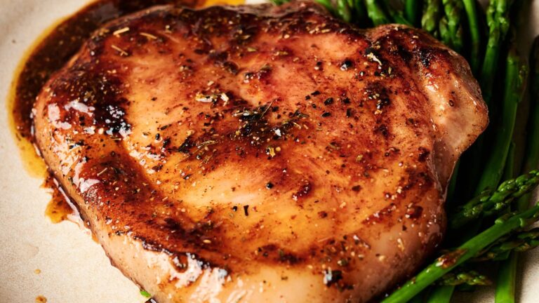 A cooked pork chop with visible seasoning, served on a plate with a side of asparagus spears.